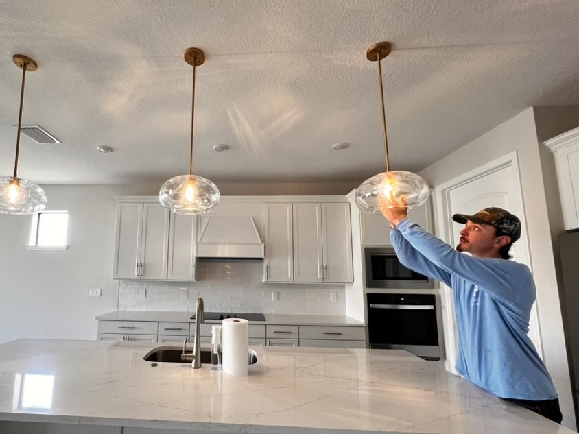 An electrician installing a glass pendant light in a kitchen